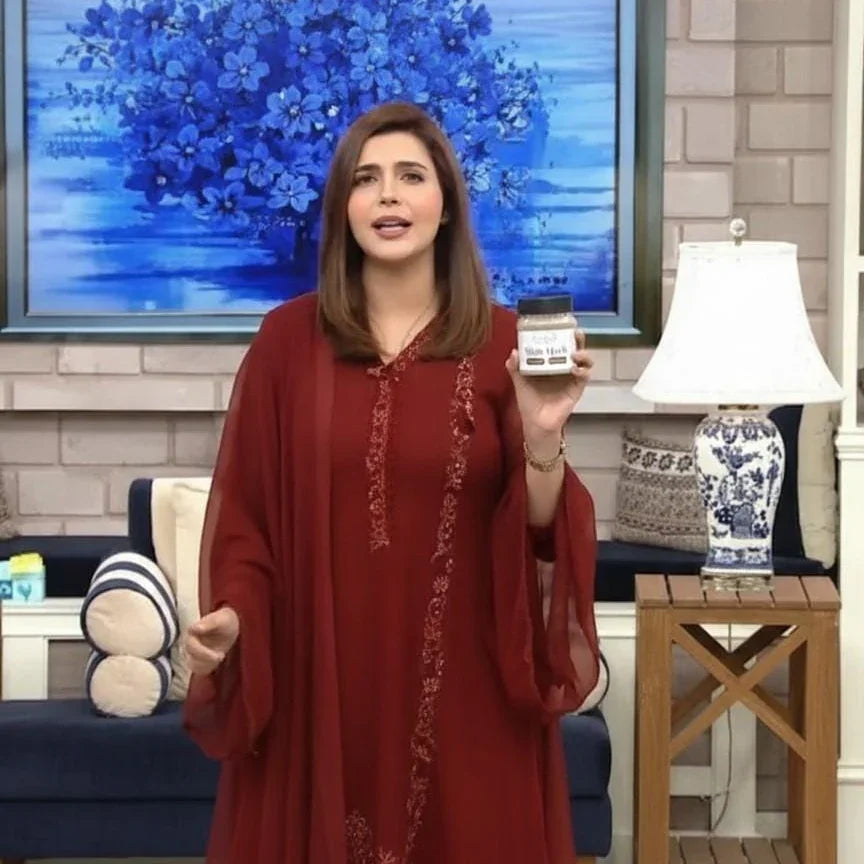 Woman in red dress presenting Black Seed jar in living room, Theshiffaa product showcase